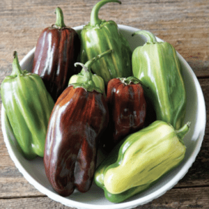 A bowl of mixed green and red peppers on a wooden surface.